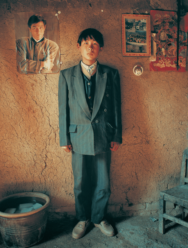 一位穿着西装的少年站在土墙前