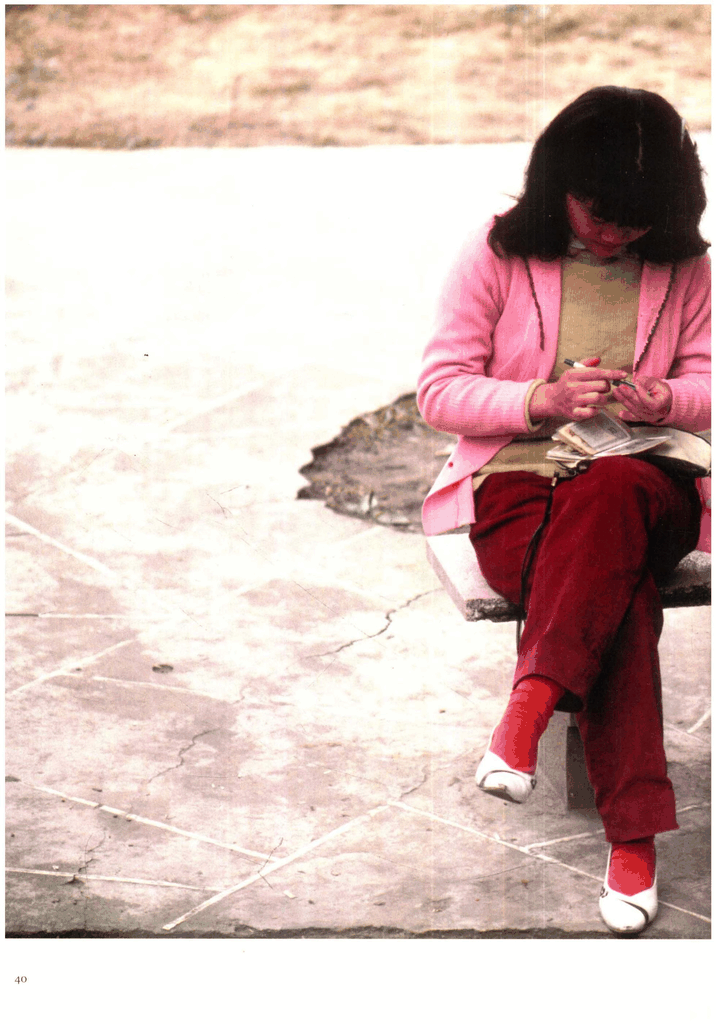 一位身着粉色开衫与红裤的年轻女子坐在石凳上低头书写