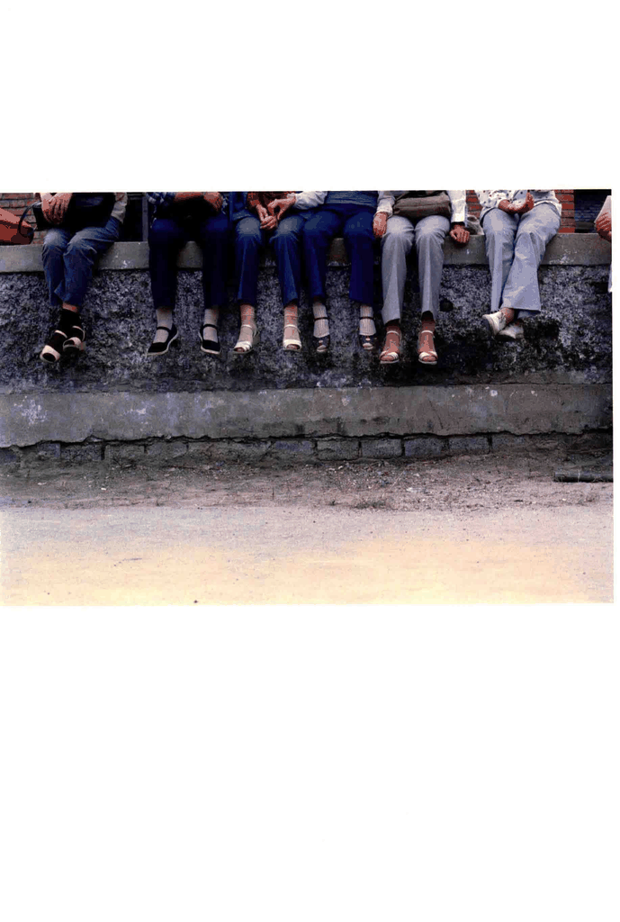 一排人坐在粗糙的水泥矮墙上，只露出了下半身和脚部