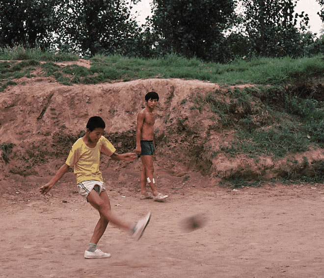 一张定格了两个男孩在土坡前踢球的怀旧照片