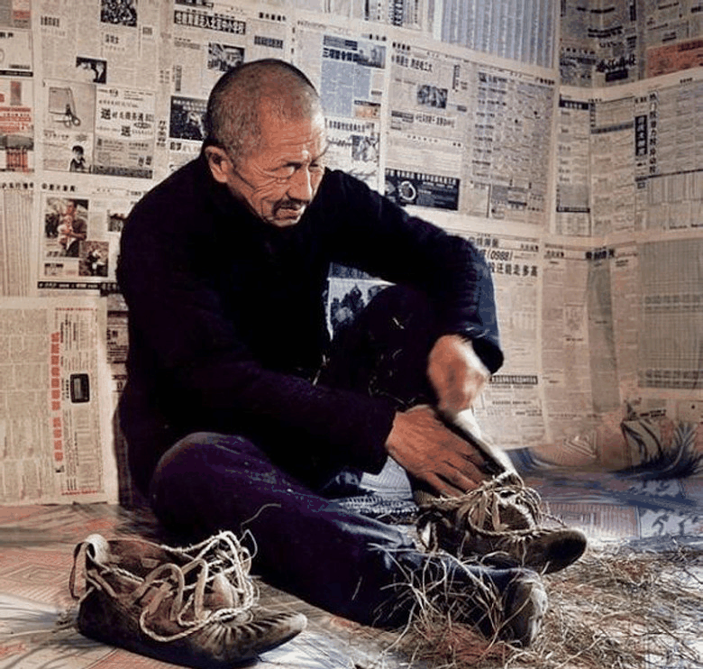 一个老人坐在贴满报纸的屋里